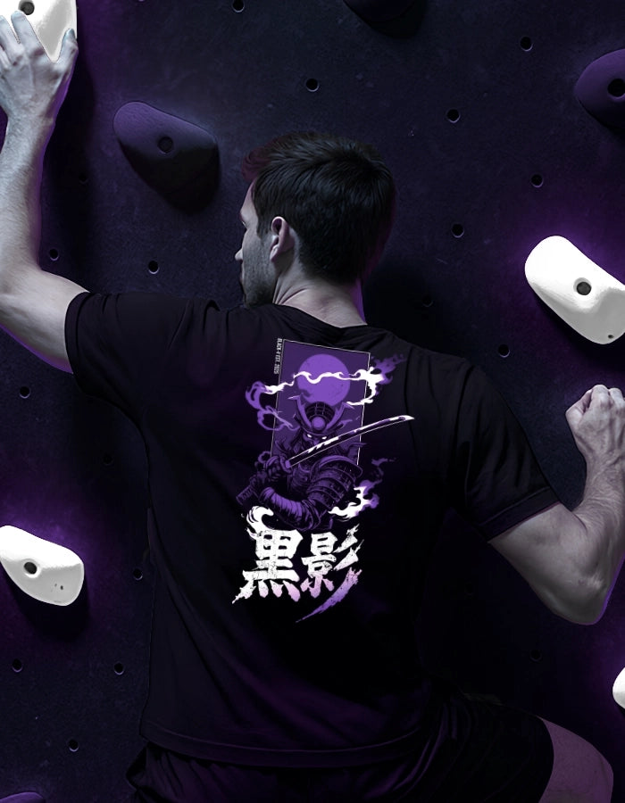 Male model rock climbing in a black T-shirt featuring a purple samurai and kanji back print. Japanese streetwear look; eco-friendly, high-quality tee. Focus on the back design.